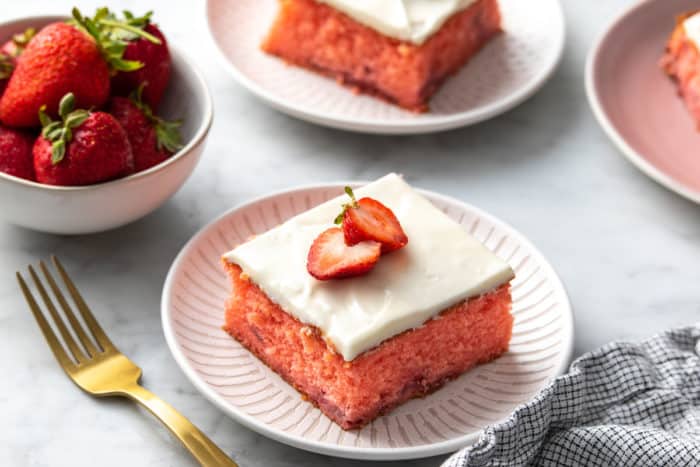 Slice of strawberry cake garnished with halved strawberries on a white plate.