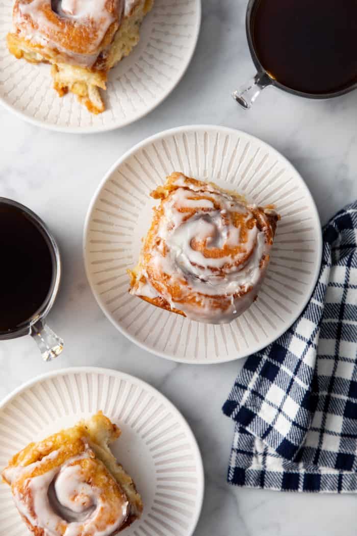 Overhead view of 3 white plates, each with a frosted cinnamon roll on it.