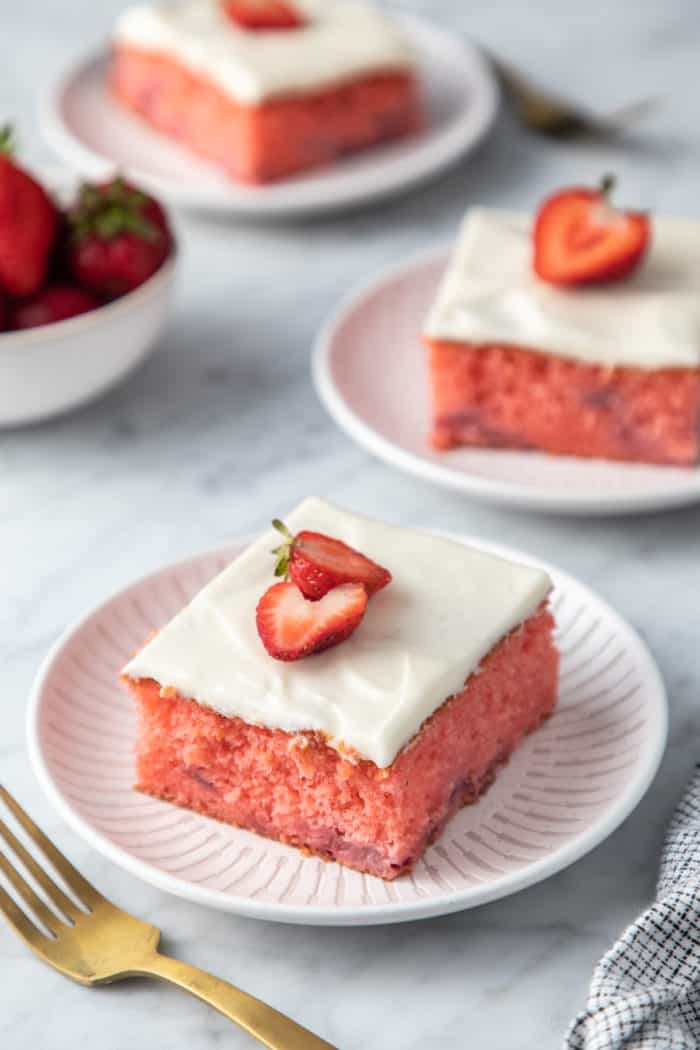 Three plates, each holding a slice of easy strawberry cake garnished with halved strawberries.