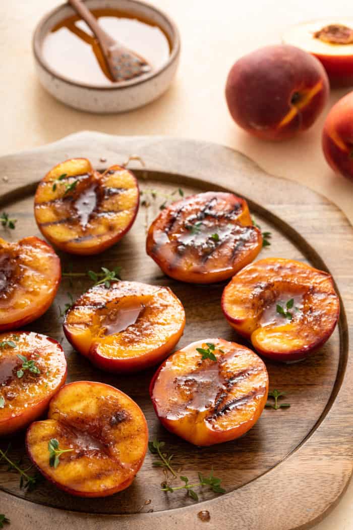 Grilled peach halves with brown sugar and thyme on a wooden platter.