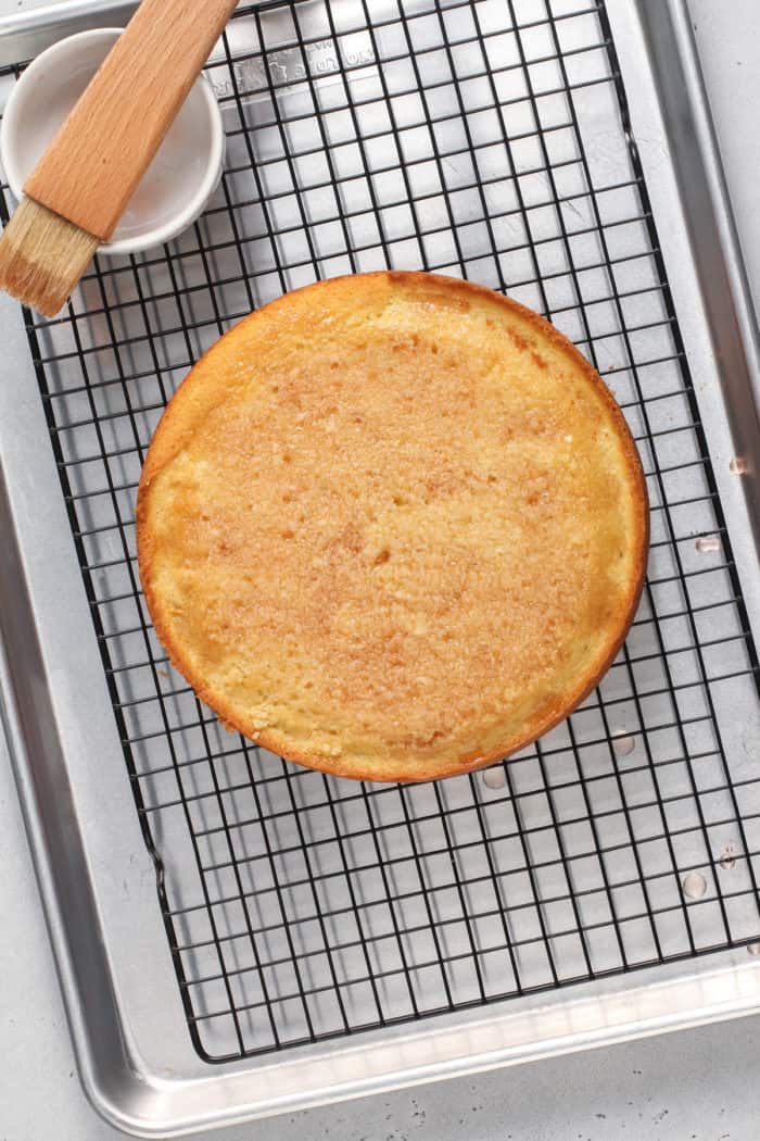 Yellow sponge cake soaked with strawberry simple syrup on a wire cooling rack.