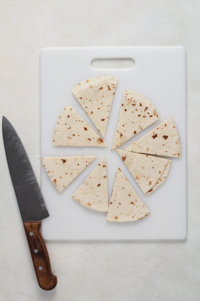 Flour tortillas cut into 8 wedges on a white cutting board.