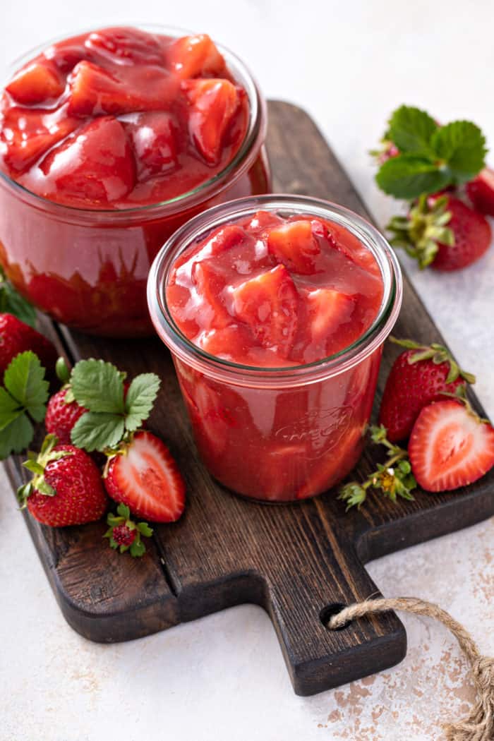 Two jars of strawberry pie filling on a wooden board.