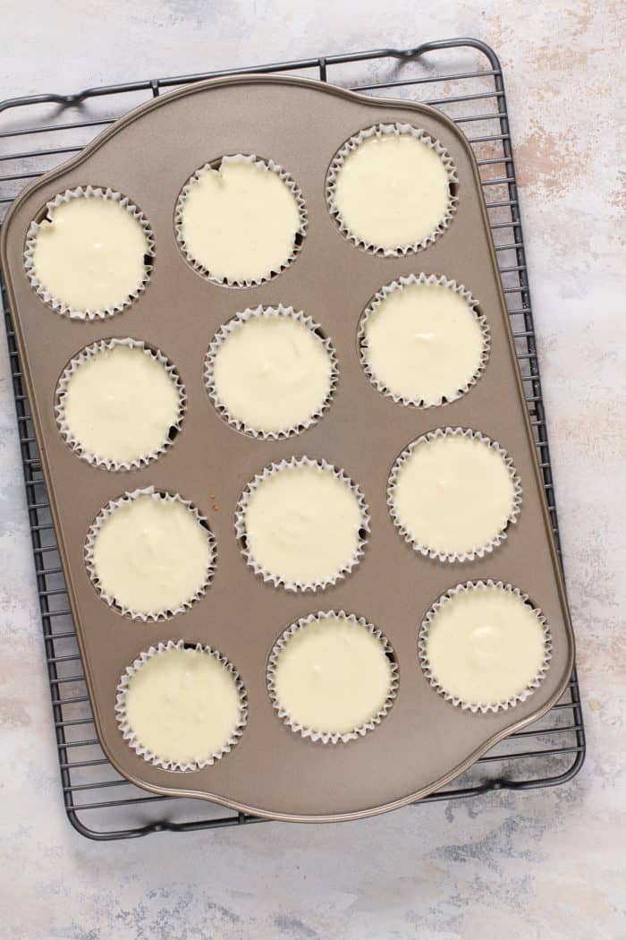 Mini cheesecakes in a muffin pan on a wire cooling rack.
