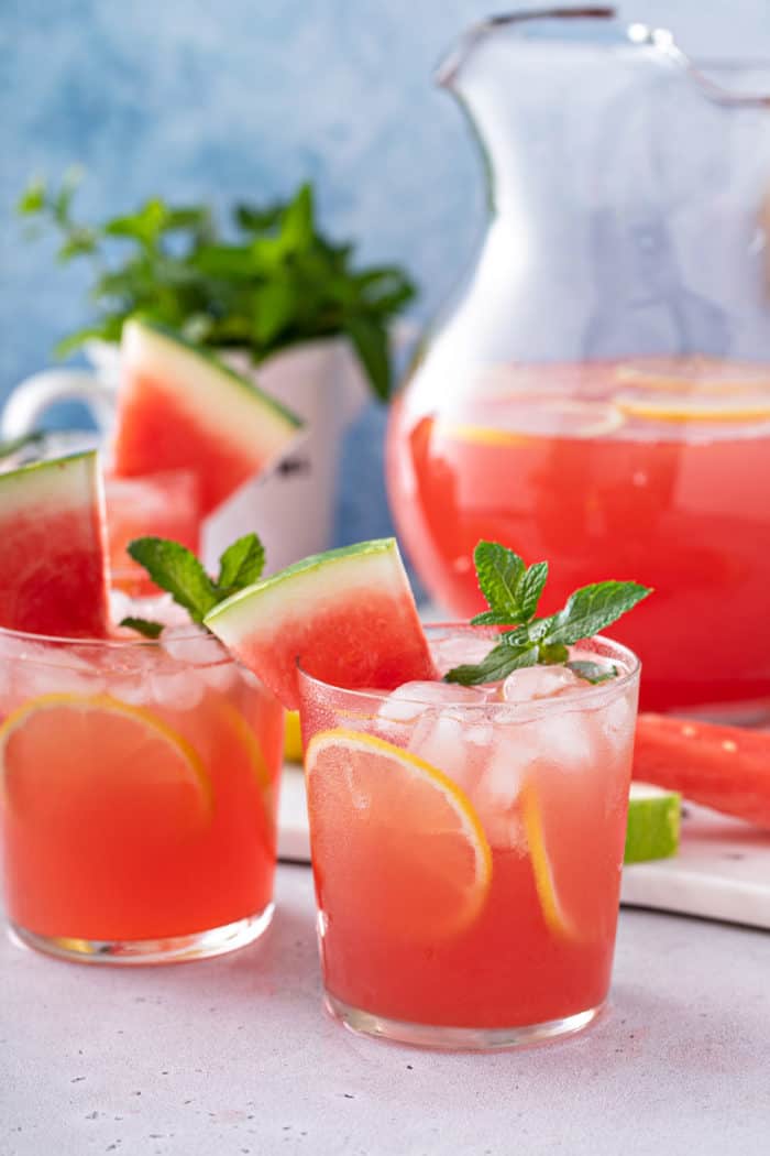 Countertop with several glasses and a pitcher of watermelon lemonade arranged on it.