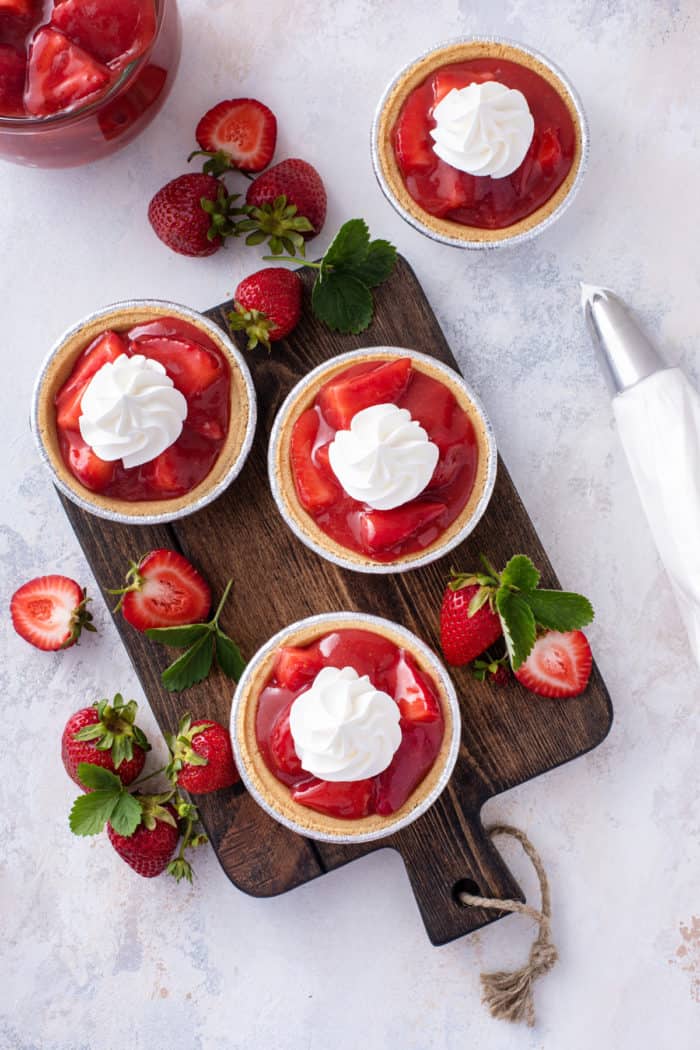 Overhead view of several mini strawberry pies topped with whipped cream.