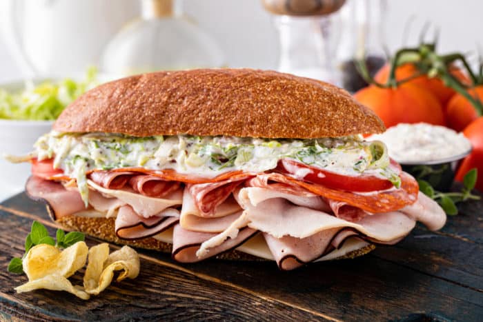 Assembled tiktok grinder sandwich on a wooden board in front of fresh tomatoes.