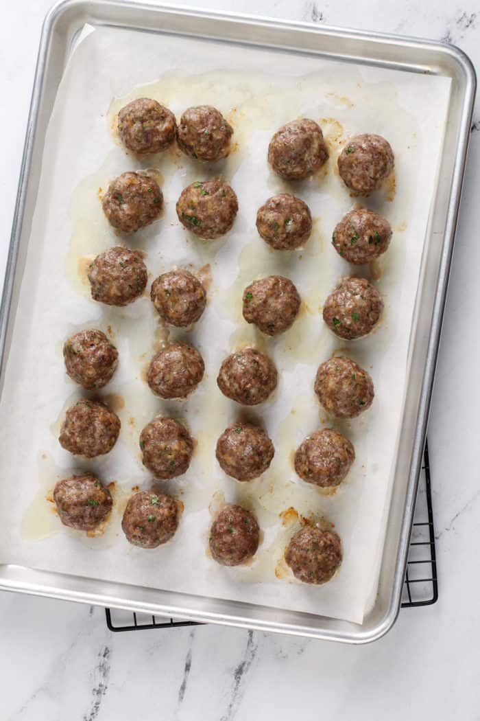 Overhead view of baked meatballs on a parchment-lined baking sheet.