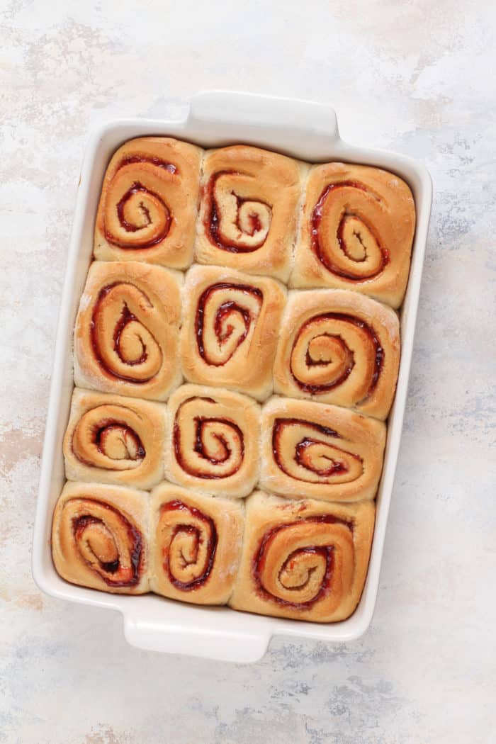Baked strawberry rolls in a white baking dish, set on a marble countertop.