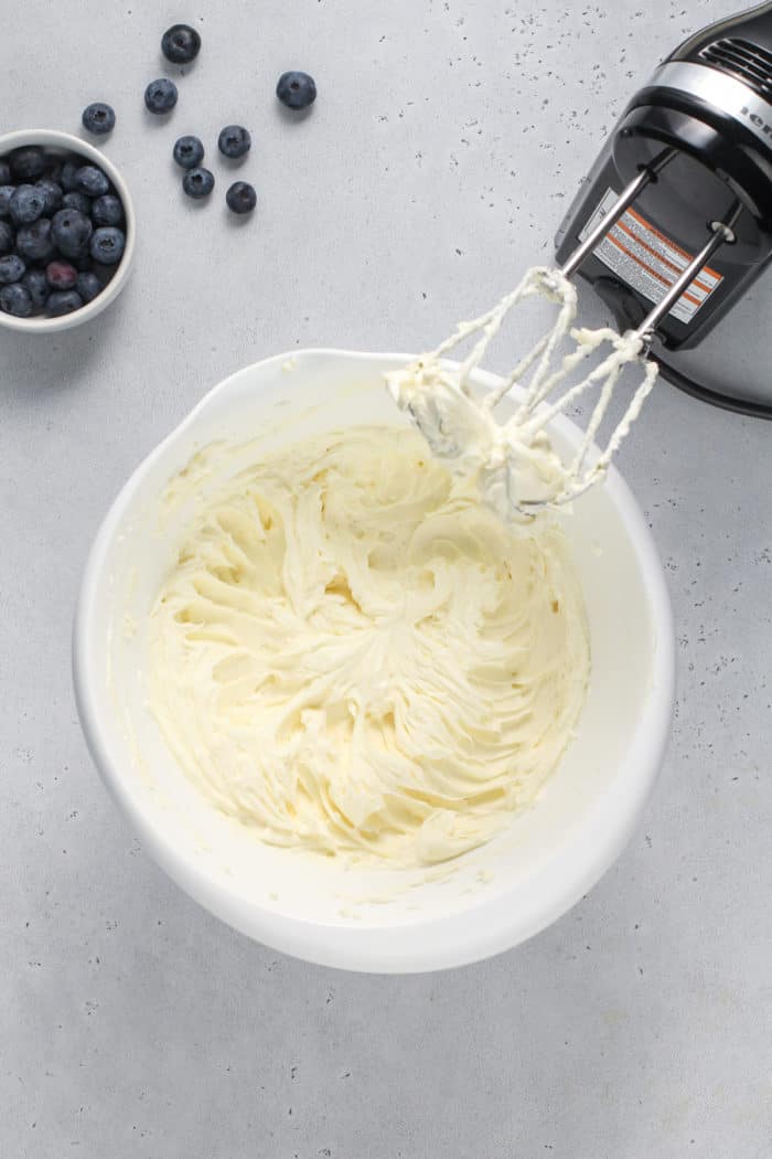 Sugar and cream cheese beaten together in a white mixing bowl.