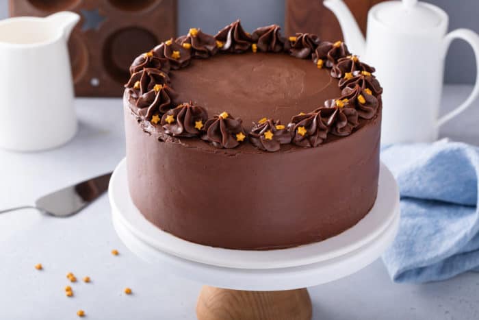 Black magic cake frosted with chocolate frosting and garnished with gold star sprinkles set on a white cake stand.