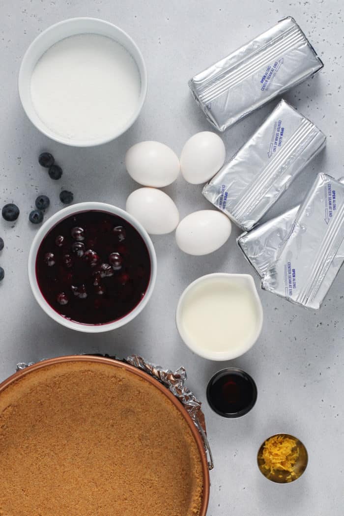 Ingredients for blueberry cheesecake on a gray countertop.