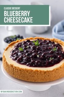 Close up of a cheesecake topped with blueberry sauce, set on a white cake plate. Text overlay includes recipe name.