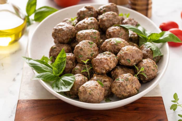 White bowl filled with homemade meatballs set on a marble and wood platter.