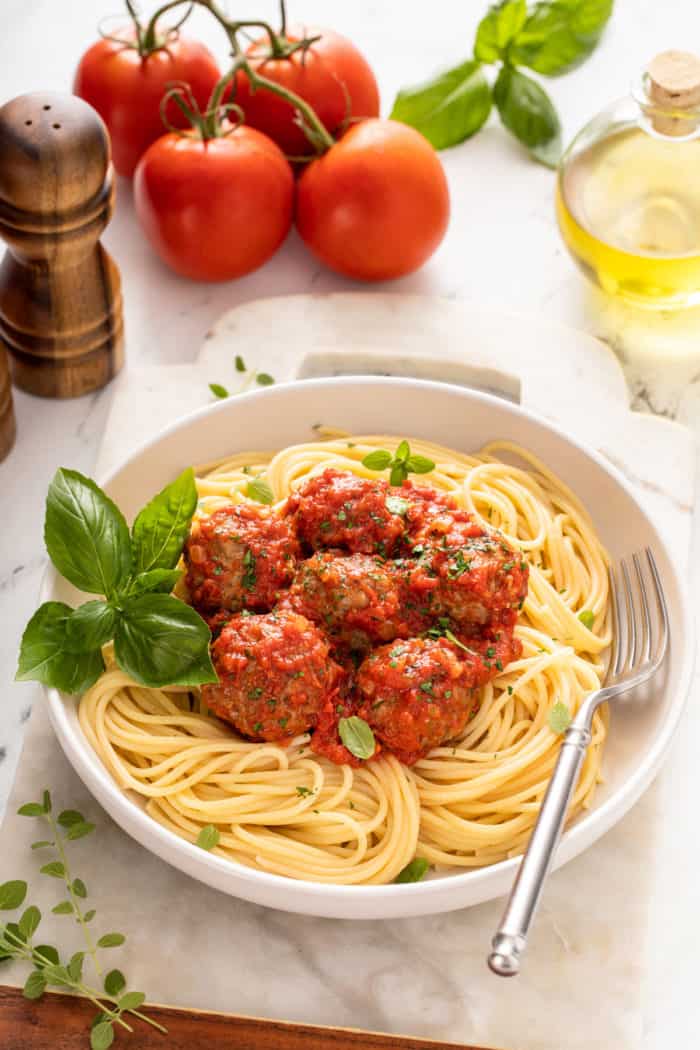 White bowl of spaghetti topped with marinara and homemade meatballs.