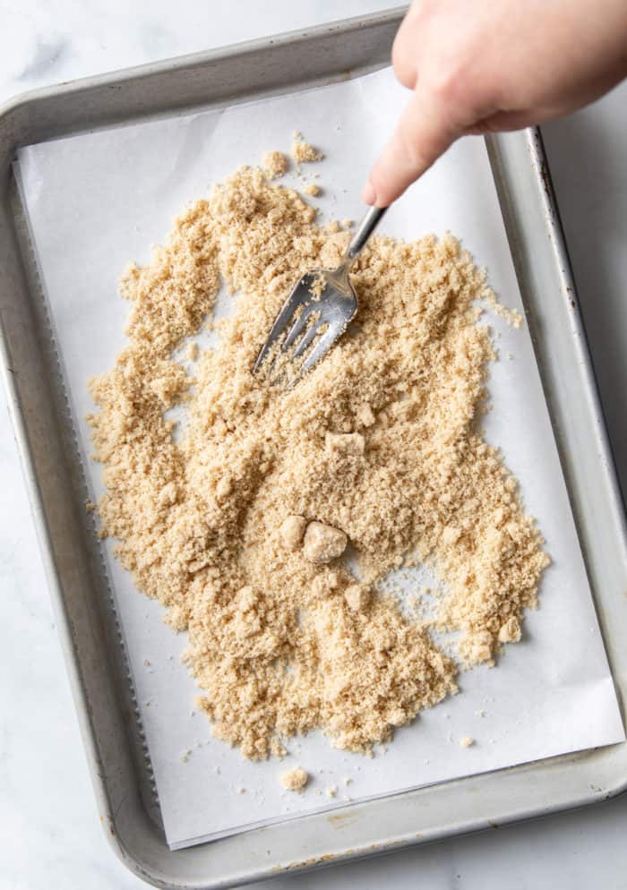 Fork stirring soft brown sugar on a parchment-lined baking sheet.