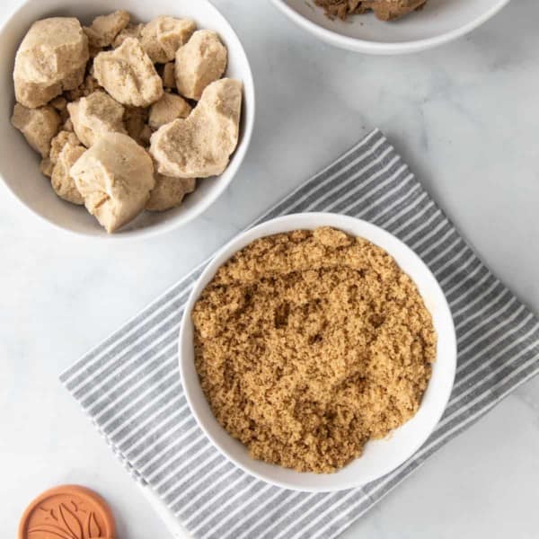 White bowls on a marble countertop. One is filled with soft brown sugar, another is filled with hard brown sugar clumps.