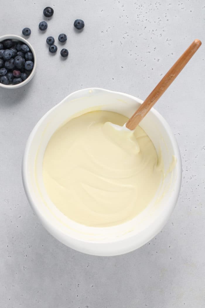 Cheesecake filling being folded with a spatula in a white mixing bowl.