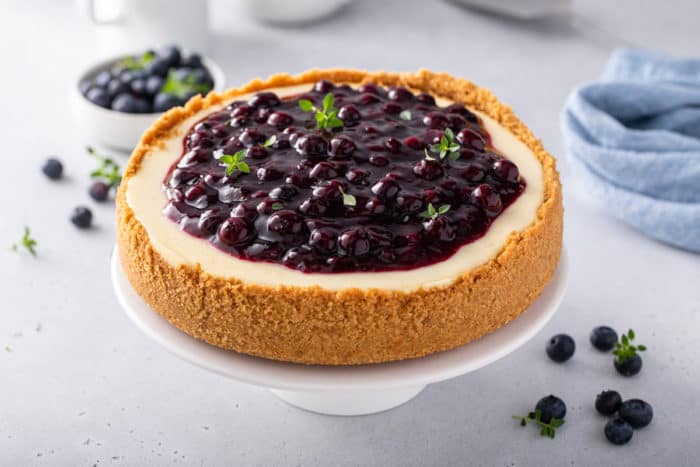 Blueberry-topped cheesecake set on a white cake plate.