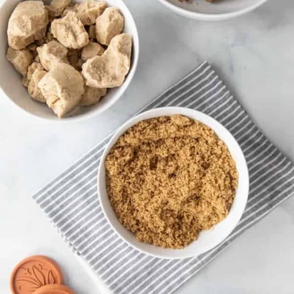 Several white bowls on a marble countertop filled with soft brown sugar and hard brown sugar clumps.