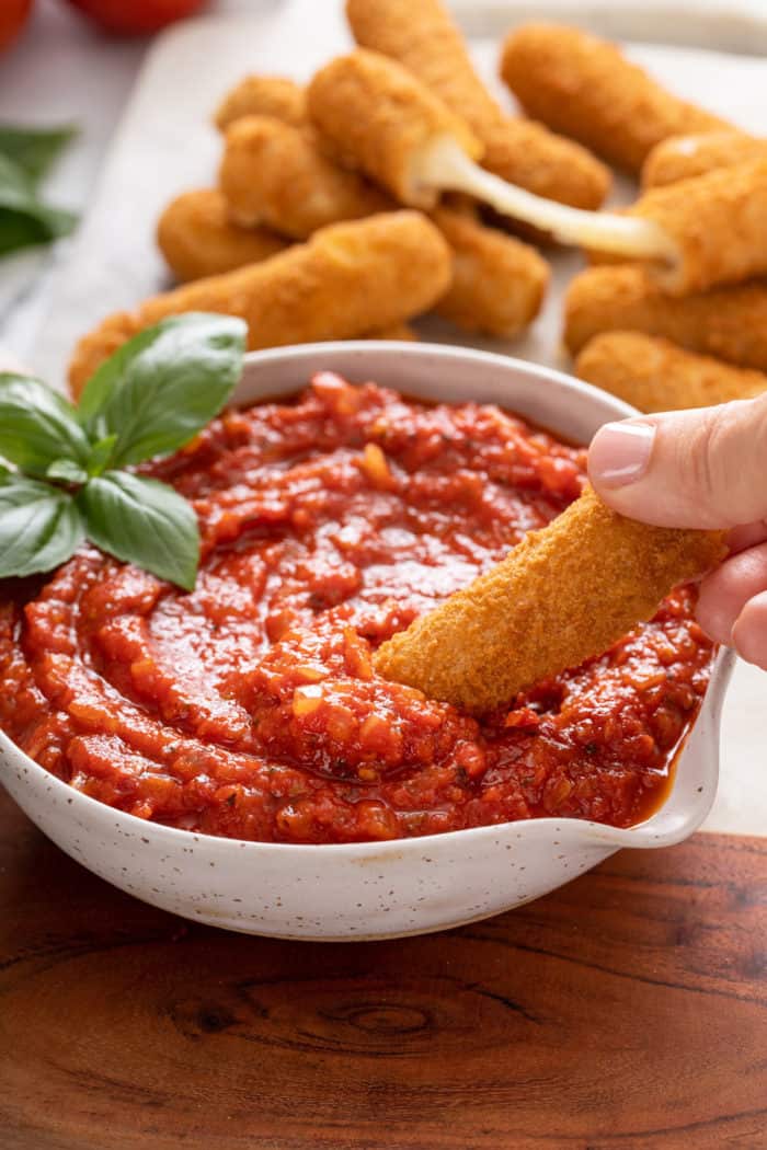 Mozzarella stick being dipped into a bowl of quick marinara sauce.