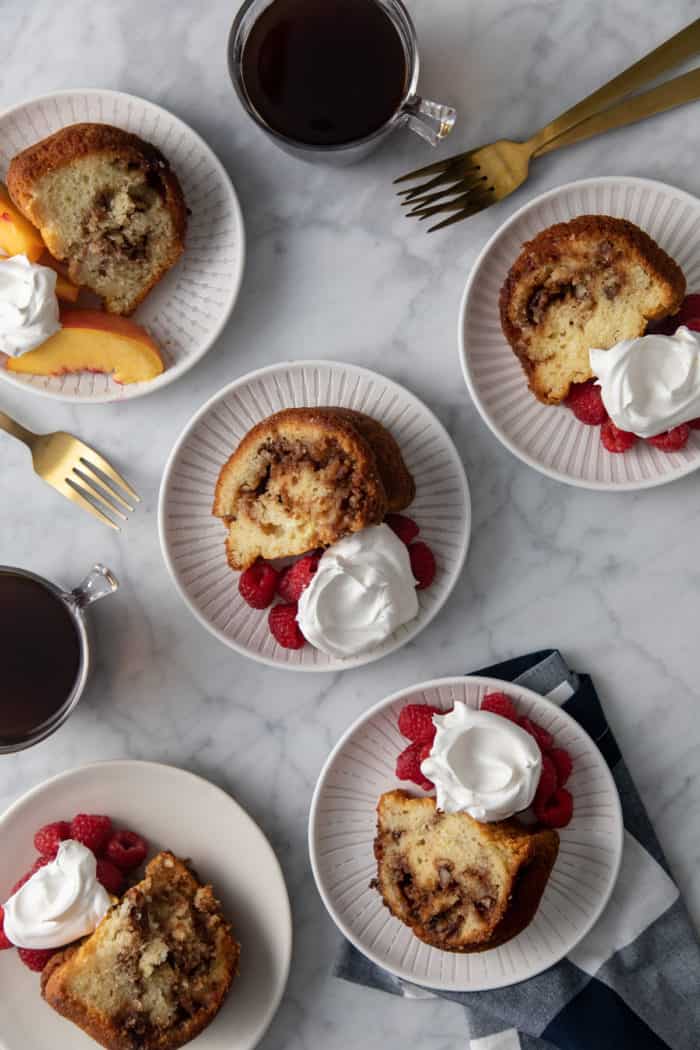 Five white plates, each holding a slice of easy coffee cake with berries and whipped cream.