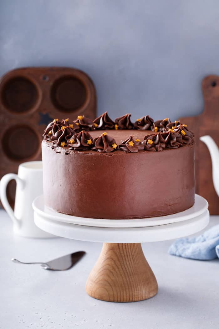 Frosted black magic cake, topped with gold star sprinkles, set on a white cake stand.