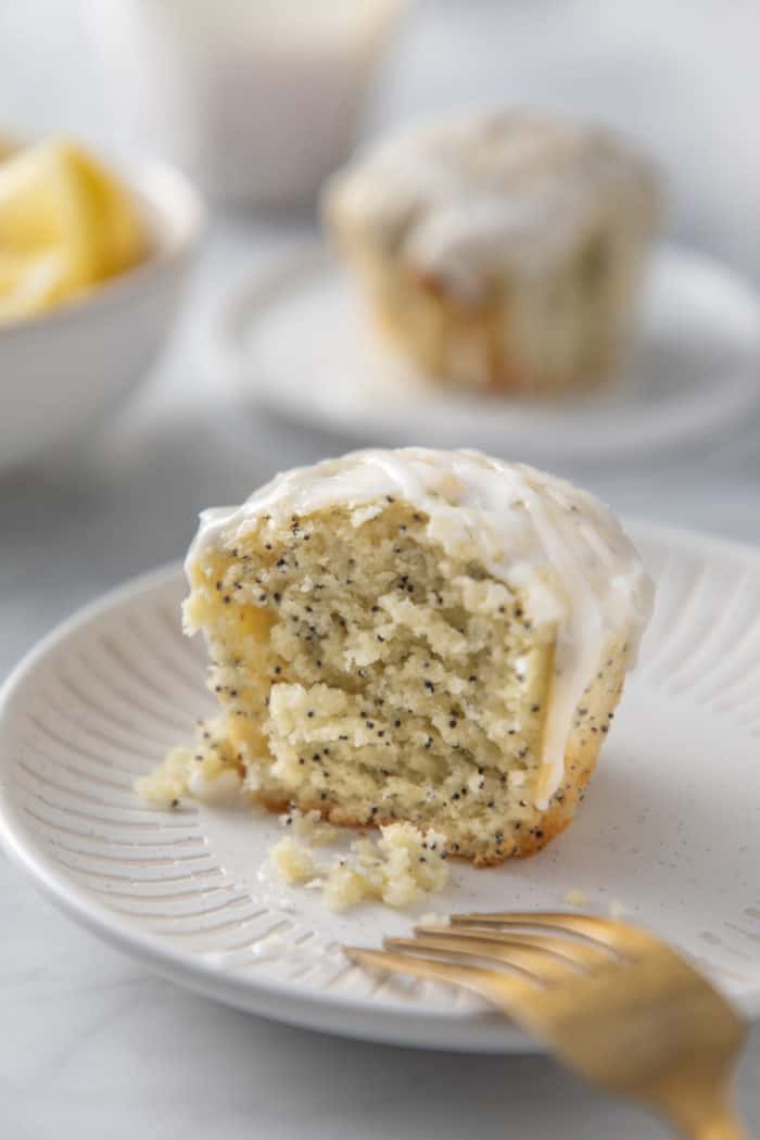 Half of a lemon poppy seed muffin next to a fork on a white plate, angled so you can see the tender crumb of the muffin.