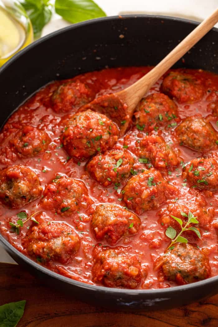 Homemade meatballs in a pan of marinara sauce being stirred with a wooden spoon.