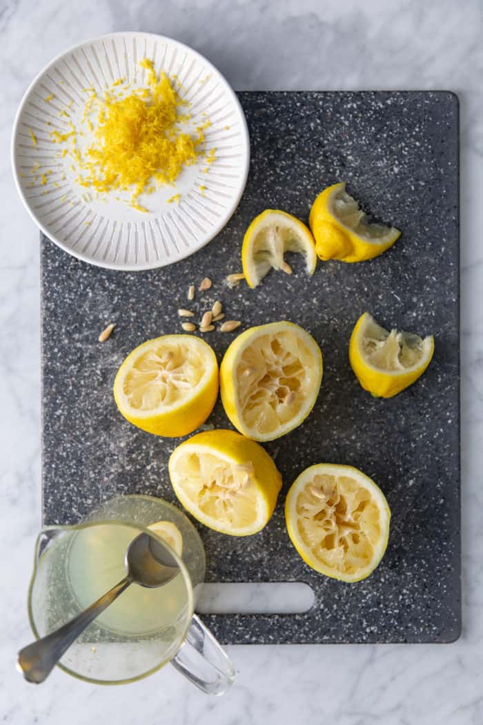 Lemons on a cutting board being zested and juiced.