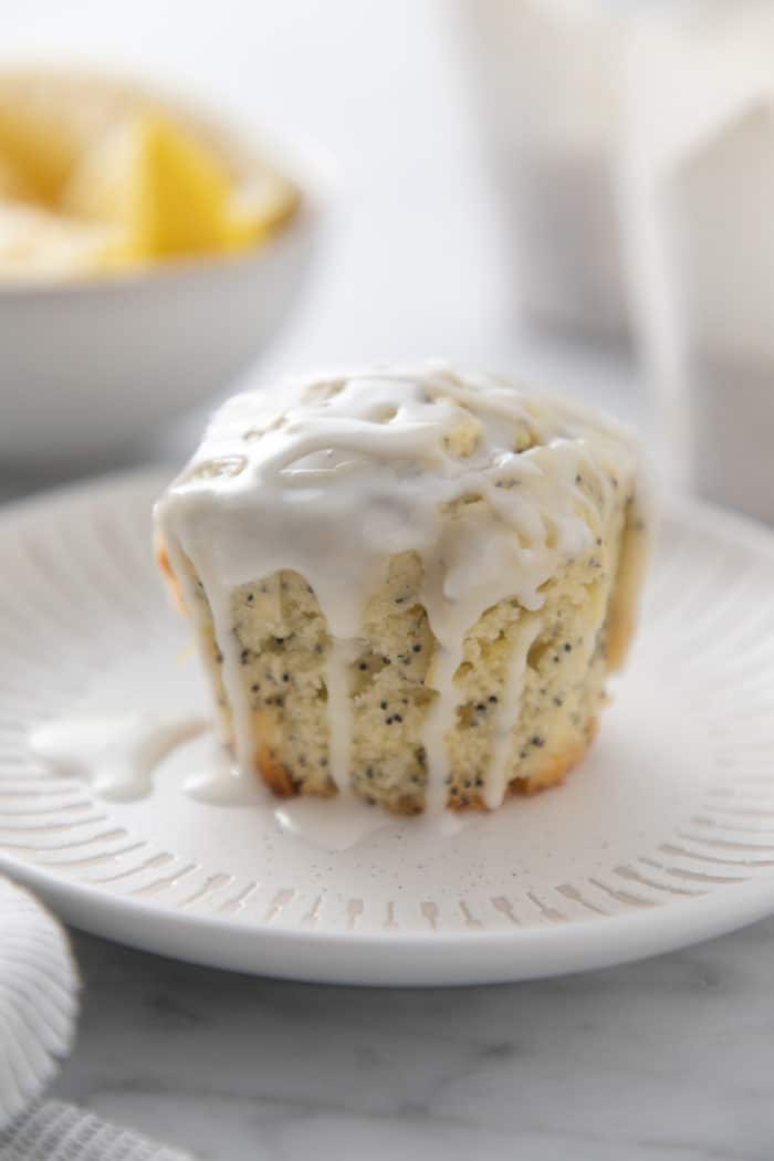 Side view of a lemon poppy seed muffin topped with lemon glaze on a white plate.