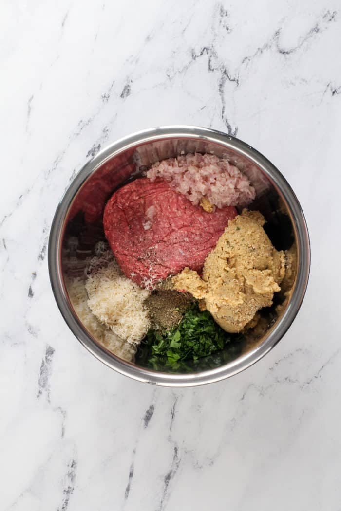 Ingredients for meatballs in a metal mixing bowl.