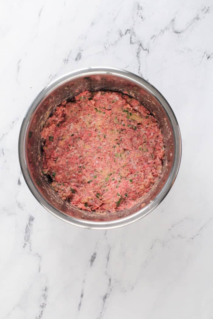 Meatball meat mixture in a metal mixing bowl set on a marble countertop.