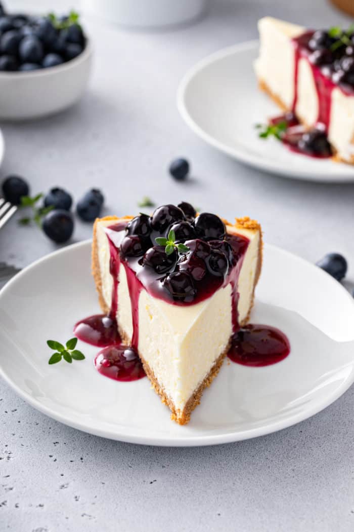 Slice of cheesecake on a white plate, topped with blueberry sauce.