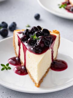 Slice of cheesecake facing the camera, topped with blueberry sauce.