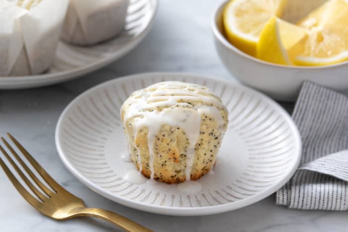 Glazed lemon poppy seed muffin set on a white plate.