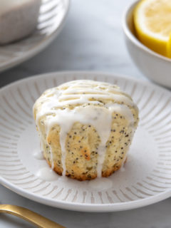 Glazed lemon poppy seed muffin set on a white plate.