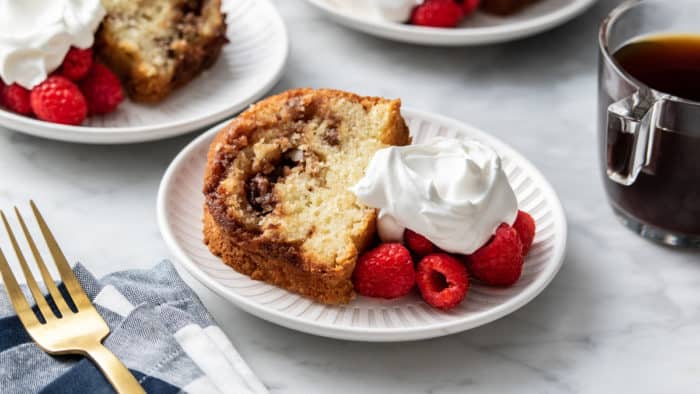 Slice of coffee cake next to fresh berries and whipped cream on a white plate.