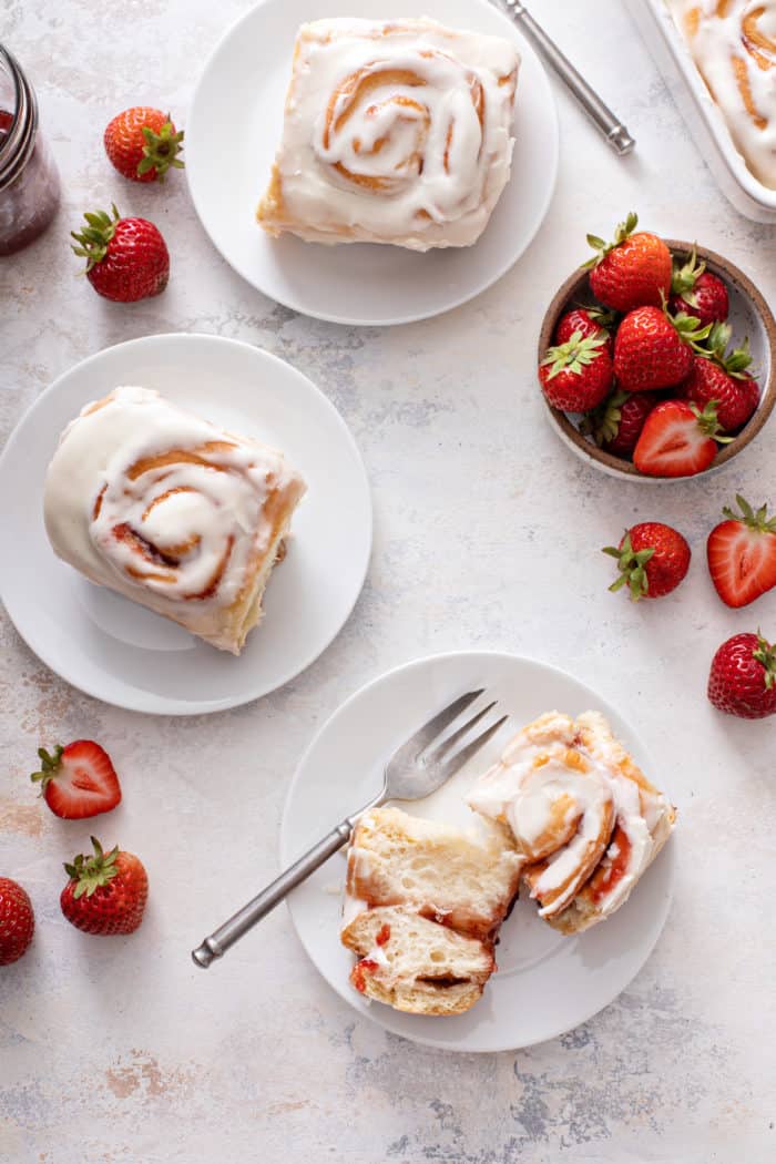 Overhead view of three white plates, each with a strawberry roll. On one of the plates, the roll is cut in half.