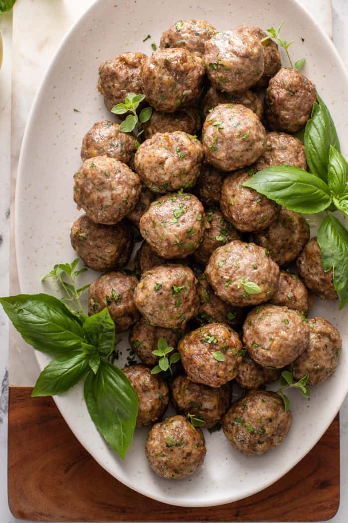 Overhead view of a white oval platter filled with baked homemade meatballs.