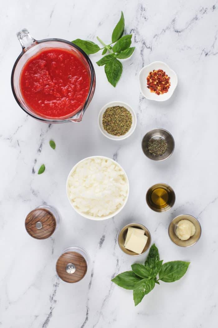 Ingredients for quick marinara sauce arranged on a marble countertop.