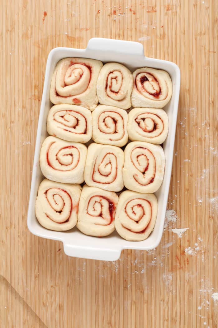 Filled, shaped, and cut strawberries rolls set in a white baking dish to rise.