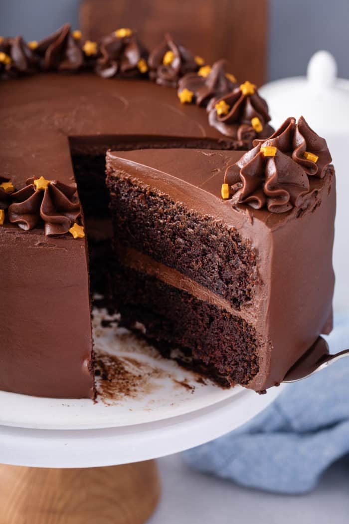 Cake server picking up a slice of black magic cake from a cake stand.