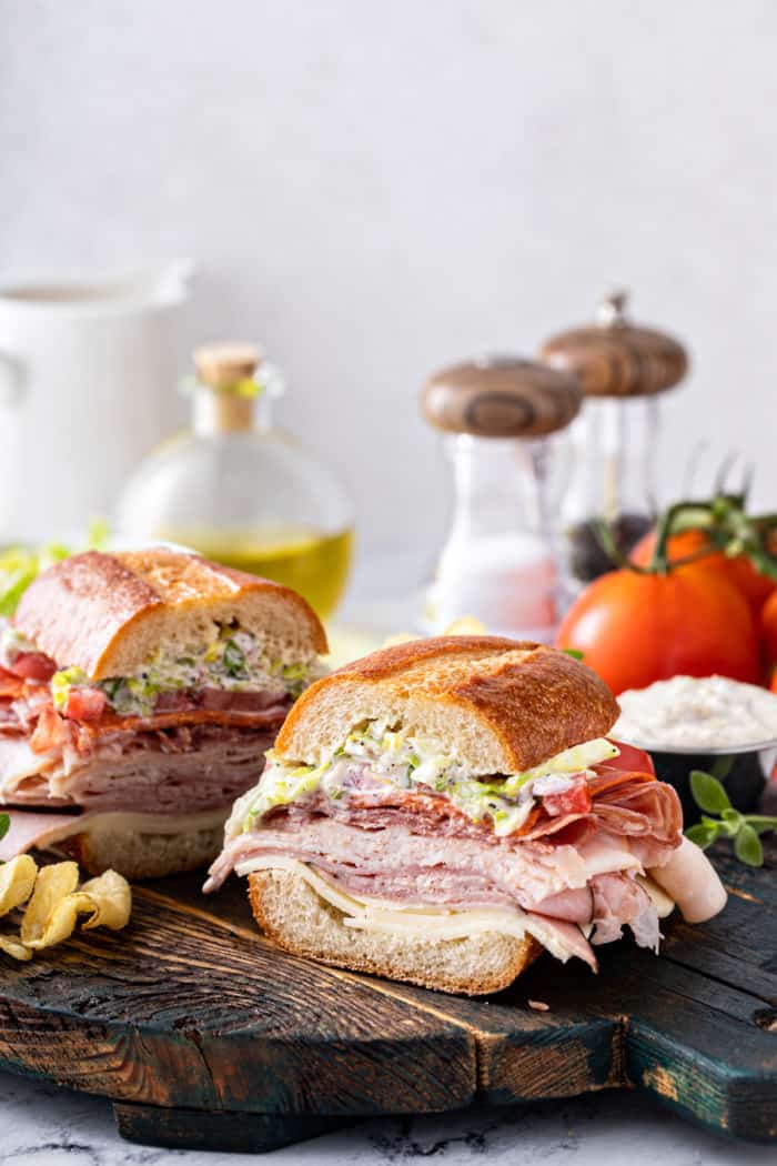 Slices of the tiktok grinder sandwich set on a wooden serving board. Salt, pepper, and tomatoes are visible in the background.