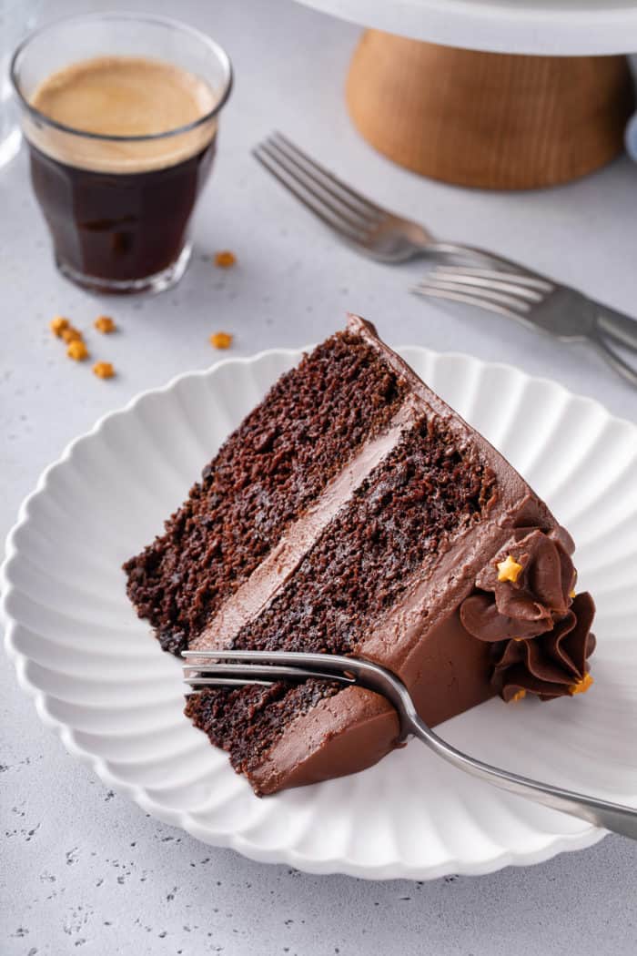 Fork about to take a bite from a slice of black magic cake on a white plate.