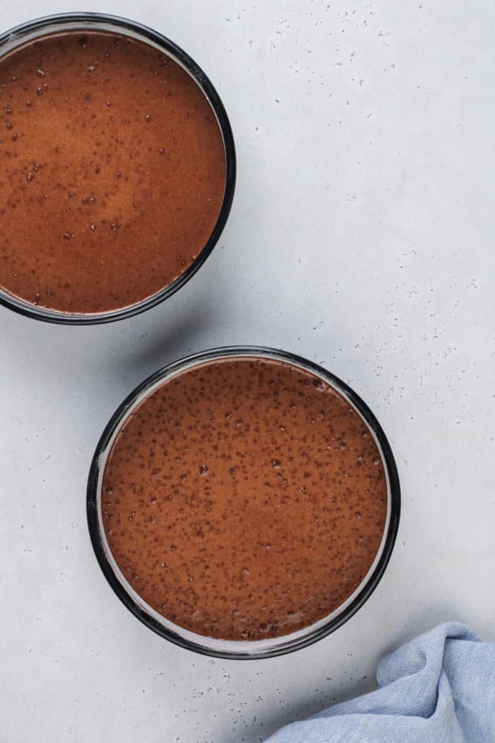 Black magic cake batter in two round cake pans, ready to go in the oven.