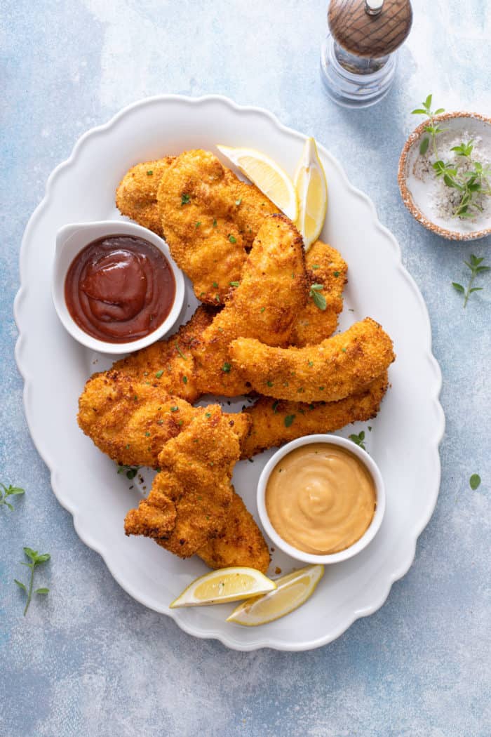 Overhead view of air fryer chicken tenders arranged on a white platter amongst bowls of dipping sauces.