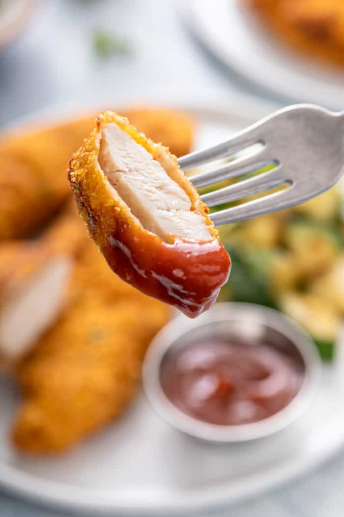 Fork holding up a bite of air fryer chicken tender, dipped in barbecue sauce.