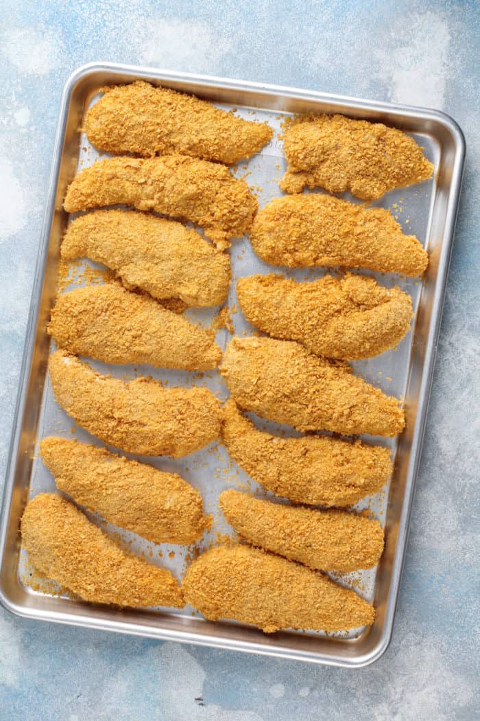 Breaded chicken tenders set on a metal sheet tray.