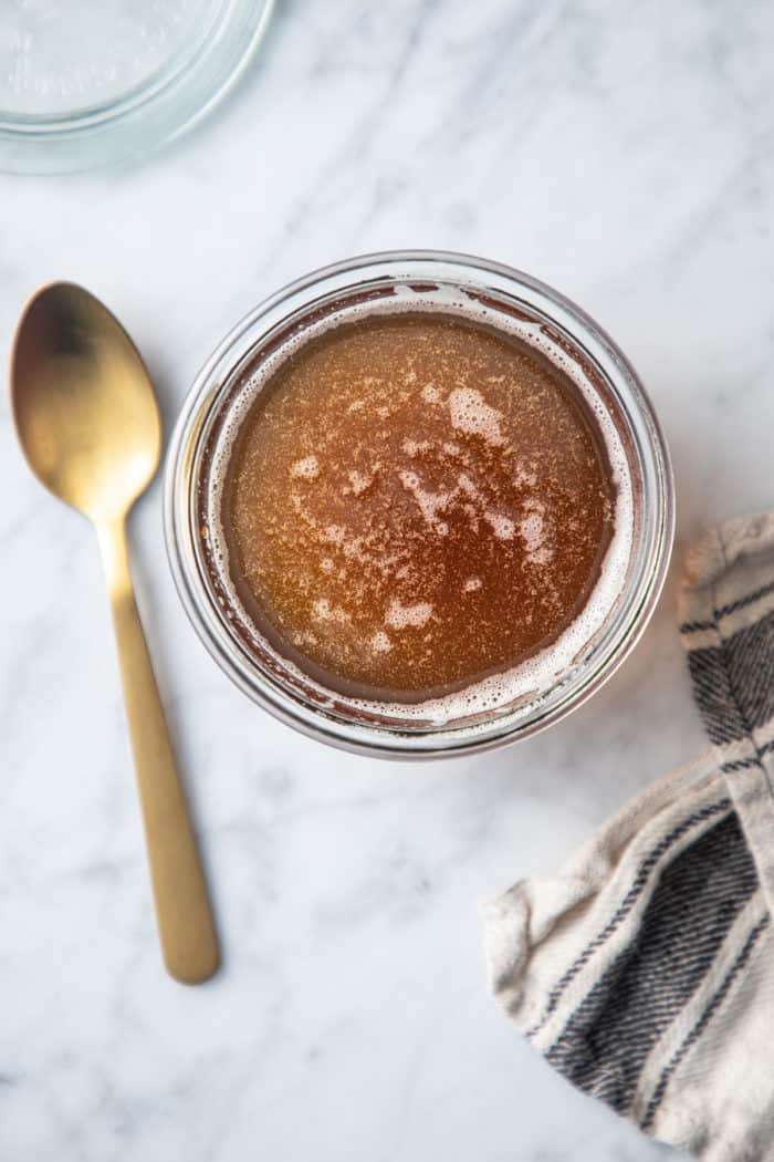 Overhead view of brown butter in a glass jar, set next to a golden spoon.
